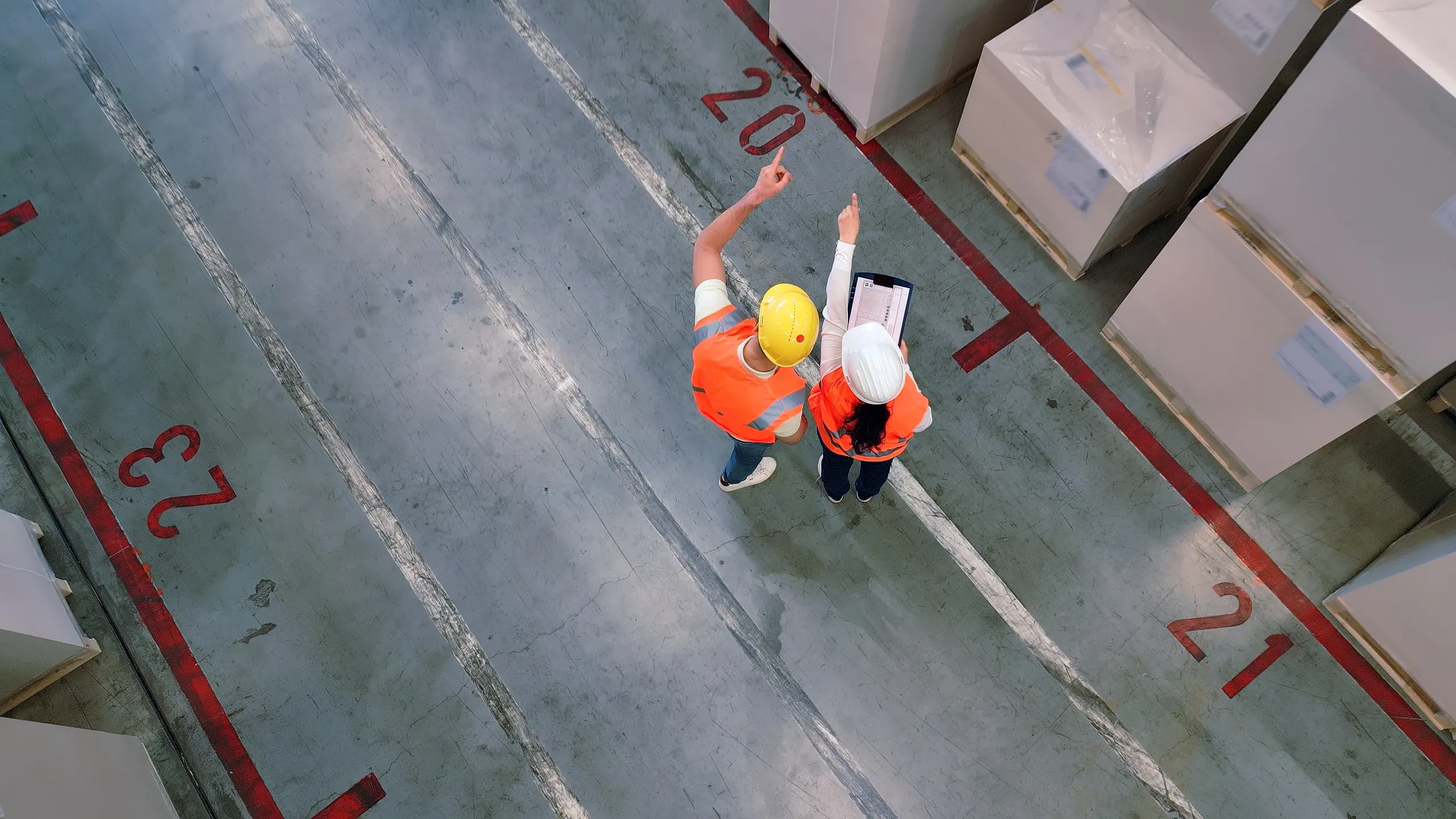 Aerial view of two warehouse workers in hard hats reviewing operations on the floor