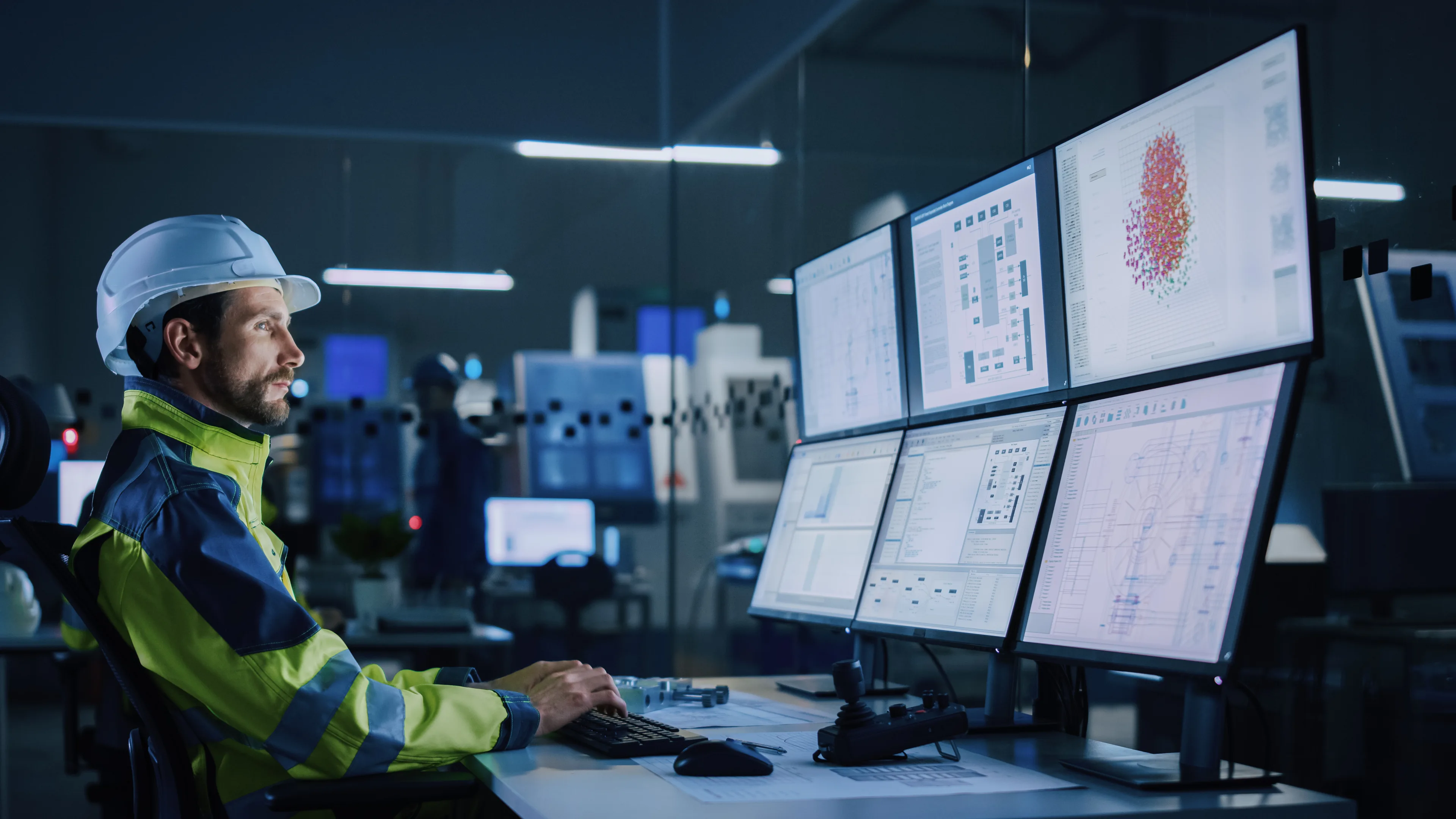 Operations leader in hard hat monitoring industrial data across multiple screens in a control room